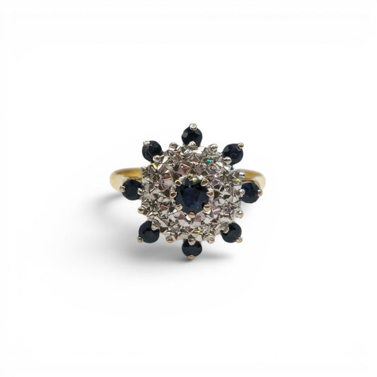 18ct yellow gold sapphire and diamond cluster ring by Reeves and Sons, showcasing a vibrant central sapphire surrounded by sparkling diamonds.