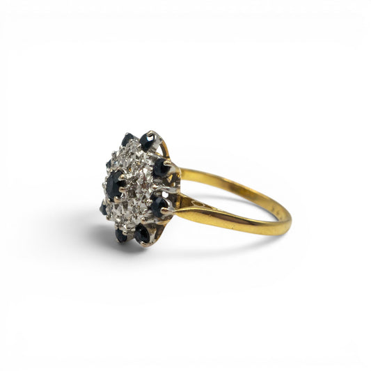 18ct yellow gold sapphire and diamond cluster ring by Reeves and Sons, showcasing a vibrant sapphire centerpiece with sparkling diamonds.