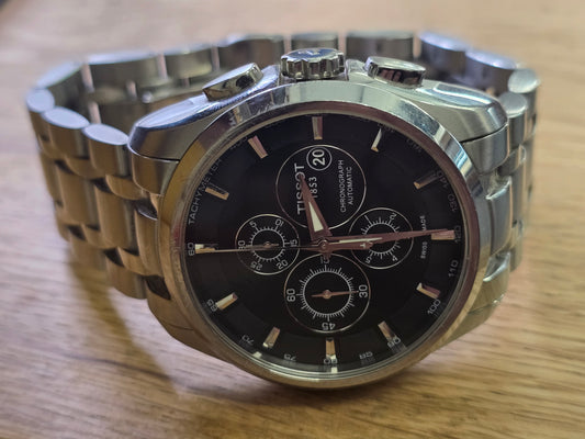 Tissot 1853 automatic chronograph watch with black dial and stainless steel bracelet, showcasing detailed watch face and bracelet design.