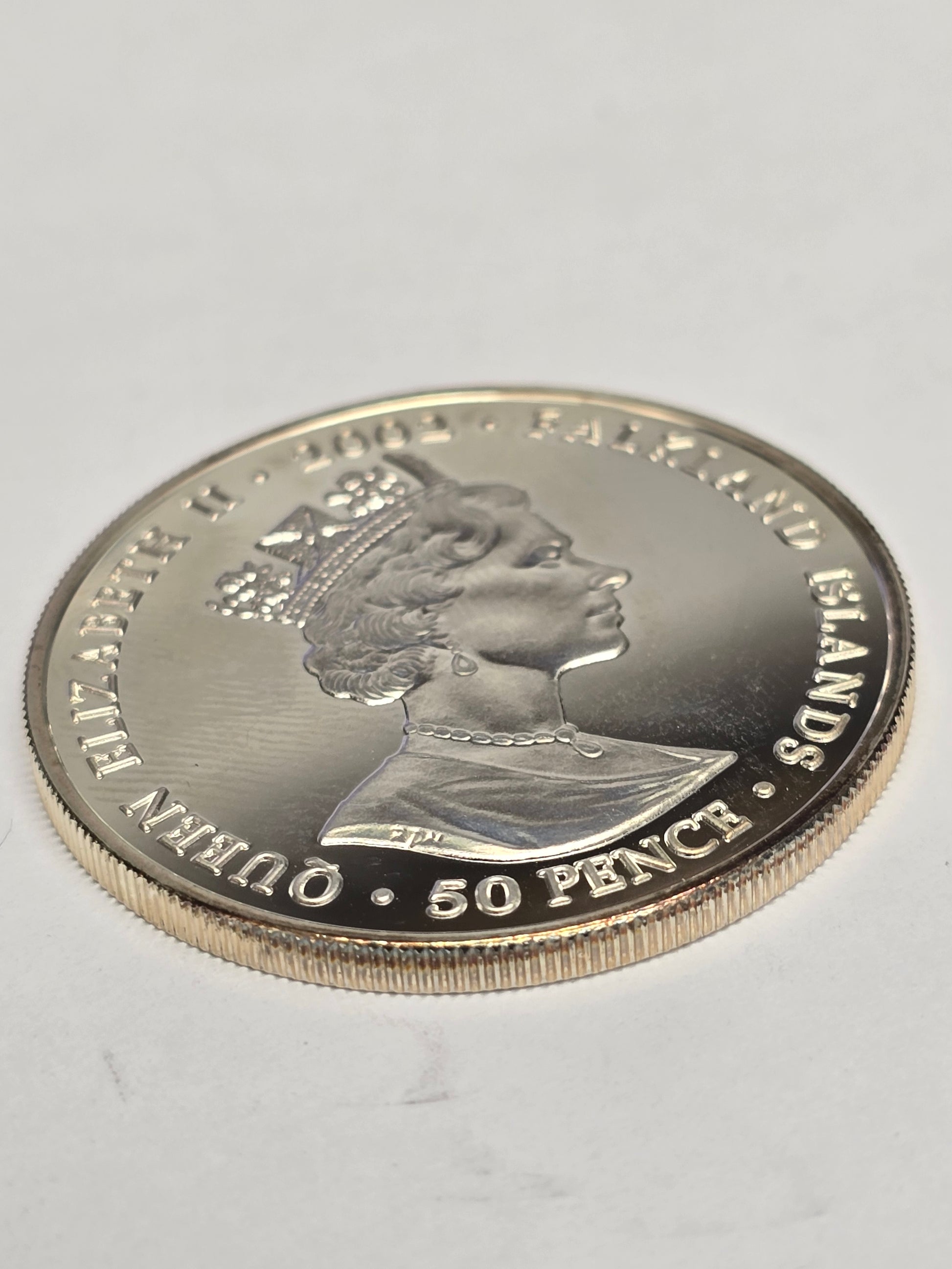 Silver 50 pence golden jubilee coin from 2002 by Reeves and Sons, showing detailed design on a shiny silver surface.