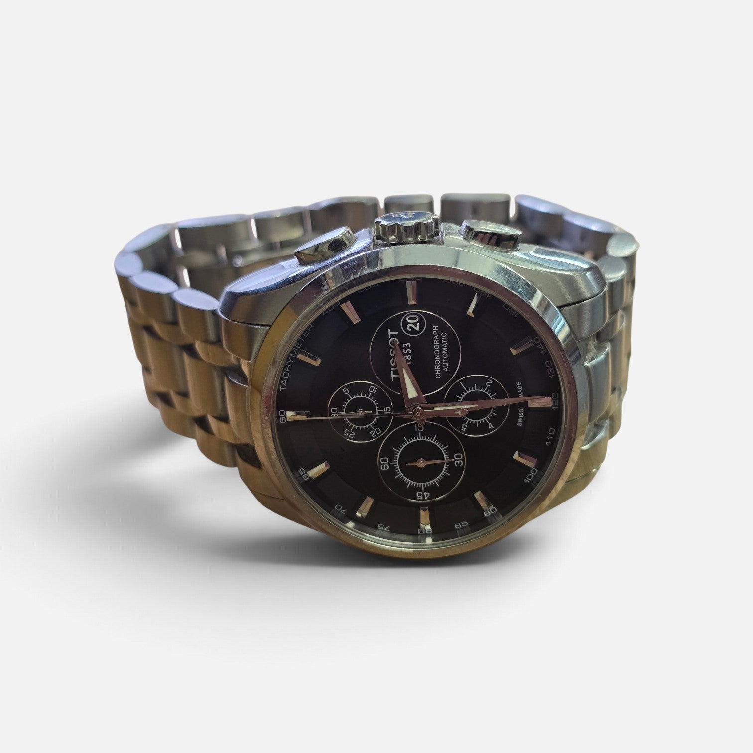 Reeves and Sons Tissot 1853 automatic chronograph watch with black dial and stainless steel bracelet on a white background.