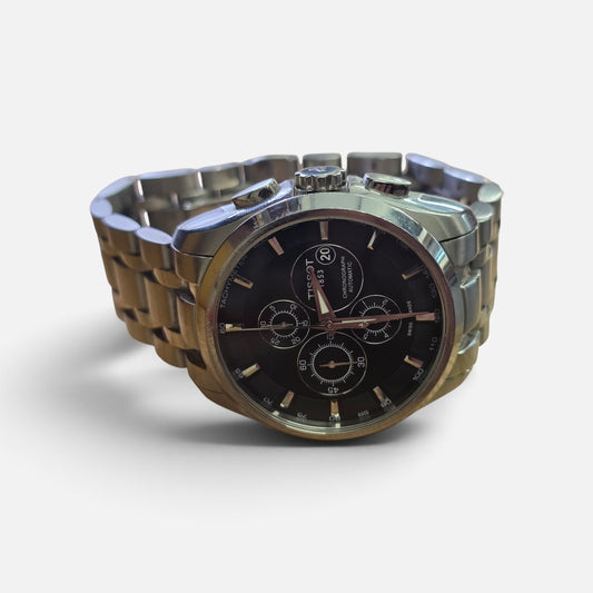 Reeves and Sons Tissot 1853 automatic chronograph watch with black dial and stainless steel bracelet on a white background.