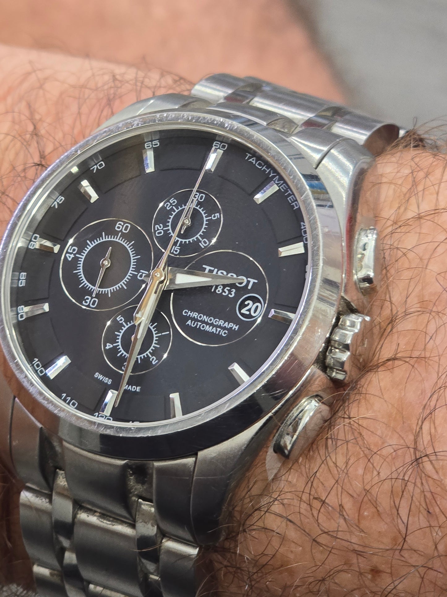 Tissot 1853 automatic chronograph watch with black dial and stainless steel bracelet, showcasing detailed watch face and bracelet links