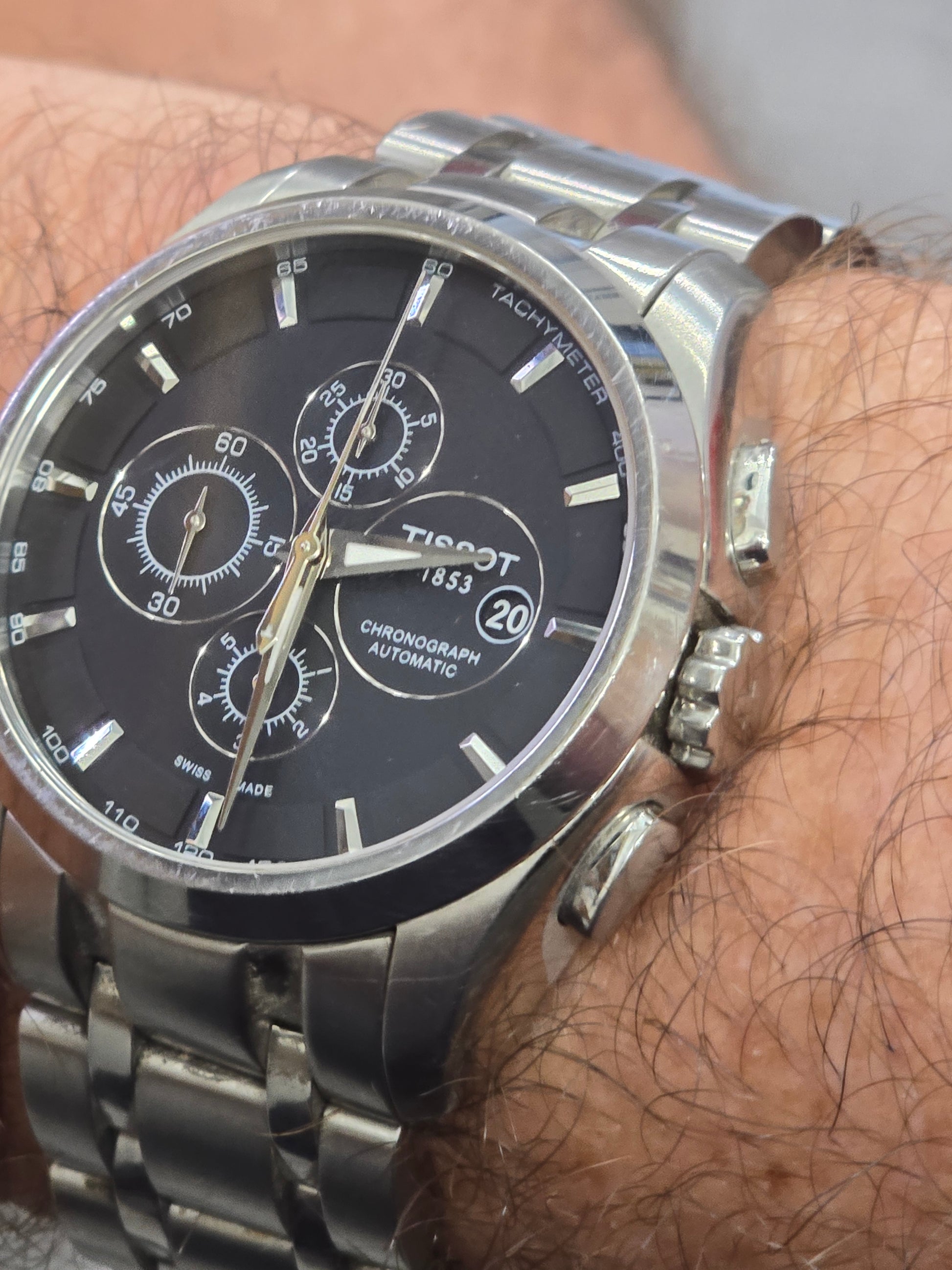 Tissot 1853 automatic chronograph watch with black dial and stainless steel bracelet, displayed on a white background