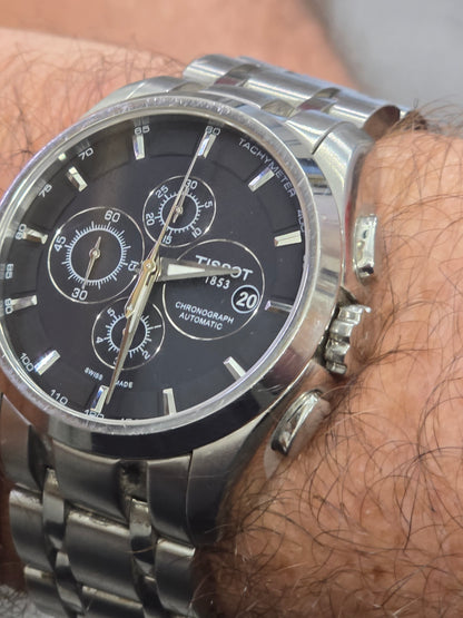 Tissot 1853 automatic chronograph watch with black dial and stainless steel bracelet, displayed on a white background