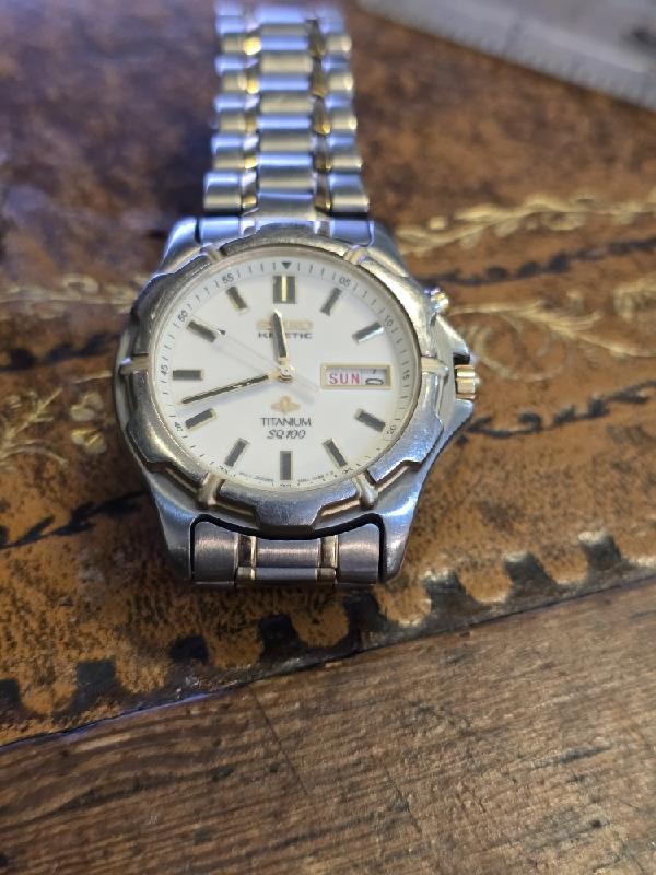 Seiko Kinetic Titanium SQ100 watch with black dial and stainless steel band, showcasing sleek design and precise timekeeping.