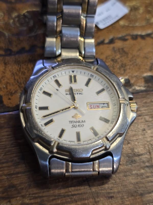 Seiko Kinetic Titanium SQ100 watch with black dial and stainless steel bracelet, showcasing sleek, modern design.
