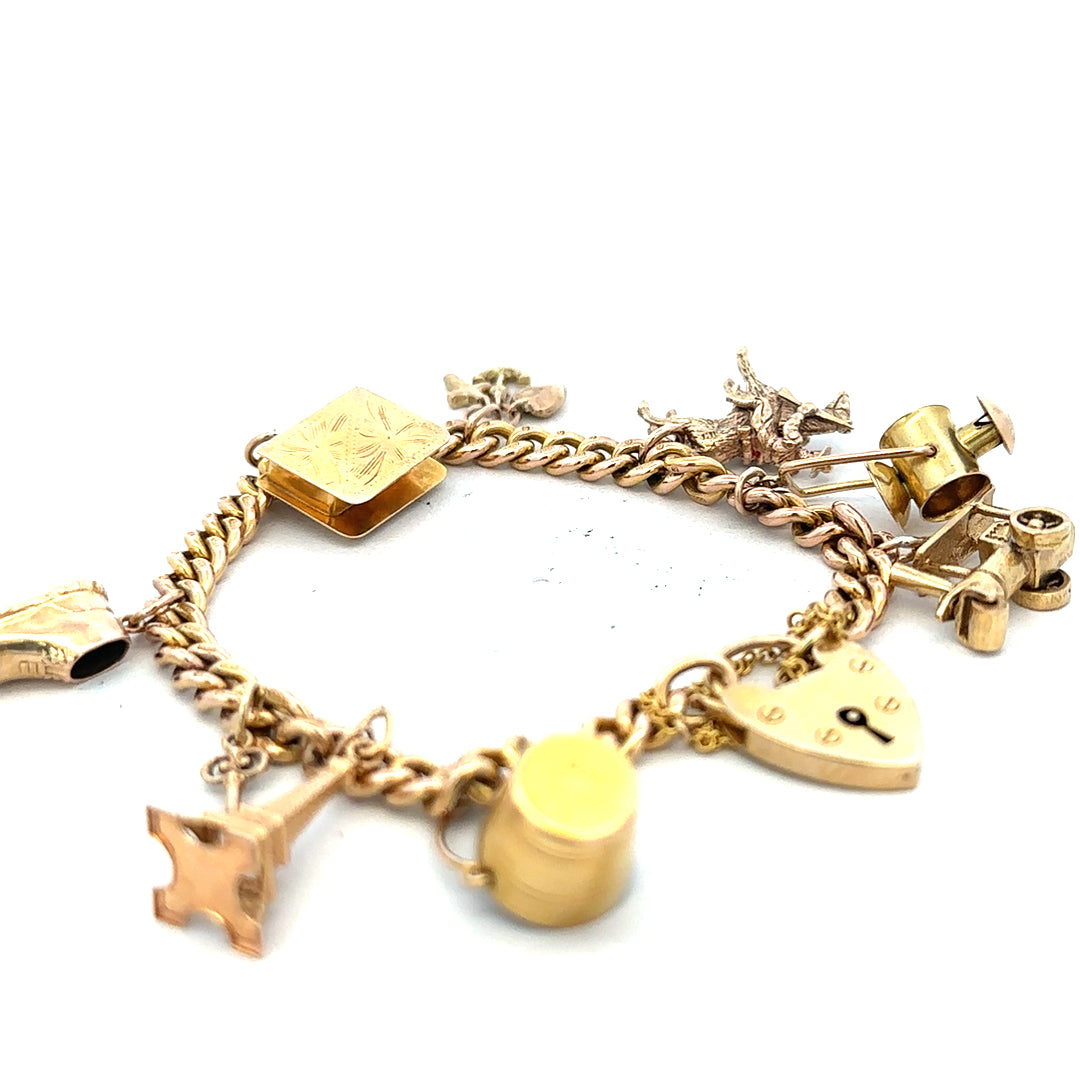 Gold charm bracelet in 9ct yellow gold, weighing 28.1g, featuring various decorative charms on a classic bracelet style.