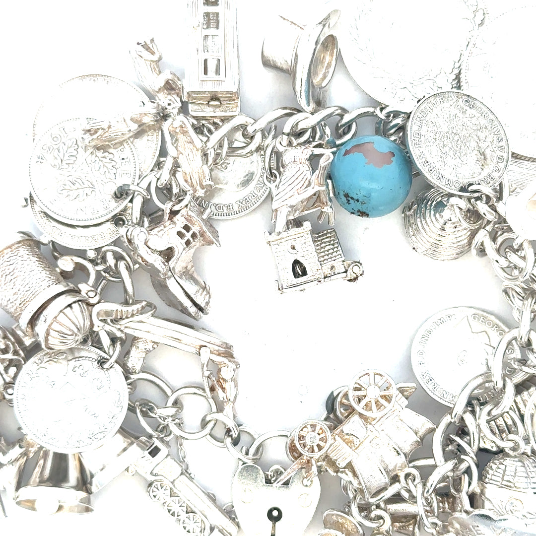 Silver charm bracelet weighing 128.8g with various charms, unbranded, showcasing detailed metalwork and elegant design.