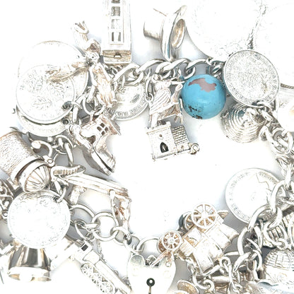 Silver charm bracelet weighing 128.8g with various charms, unbranded, showcasing detailed metalwork and elegant design.
