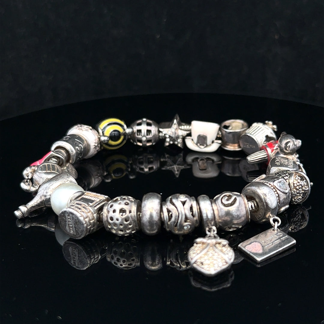 Silver charm bracelet with multiple decorative charms, unbranded, featuring a 64.8 cm length and silver finish.