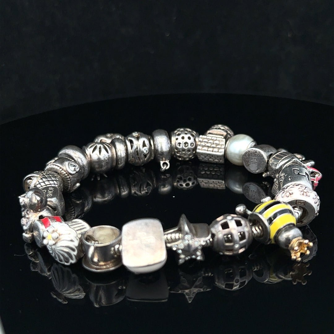 Silver charm bracelet with multiple charms, unbranded, featuring a 64.8mm length, displayed on a neutral background.
