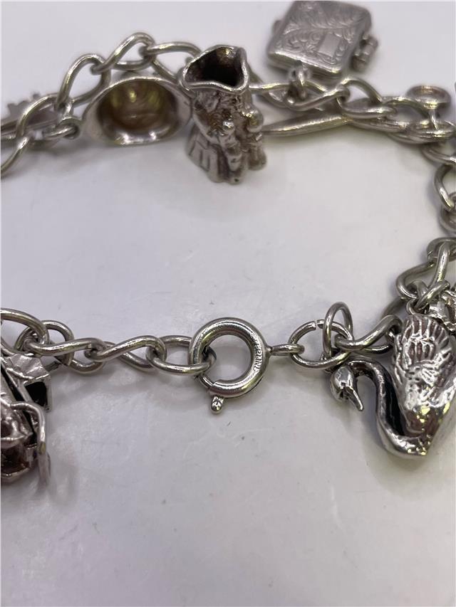 Silver charm bracelet with intricate designs, weighing 33.9g, featuring various decorative charms on a sleek bracelet.